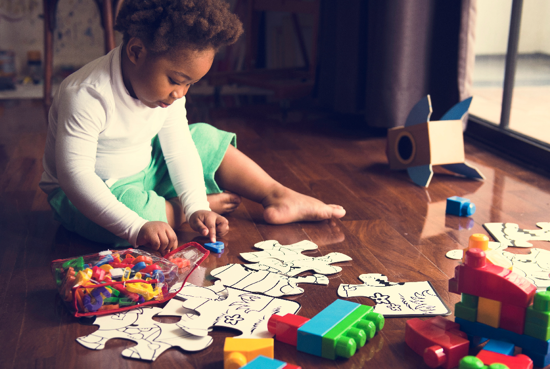 Child sitting on the floor playing with puzzle pieces, Duplo blocks and magnetic plastic letters
