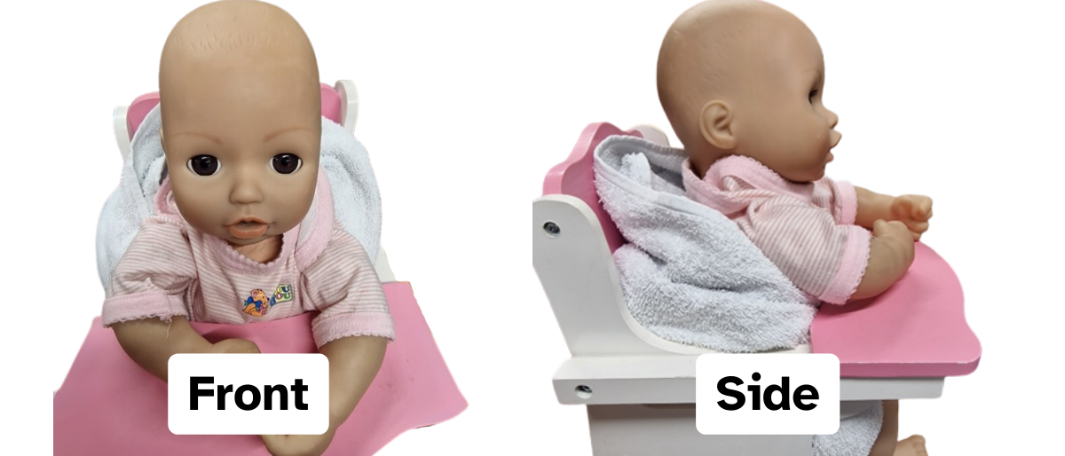 Toy baby sitting in wooden highchair with a towel rolled up and placed behind their back. The towel is between the chair and the baby's back. It is behind the shoulders gently pushing the arms forward. back and shoulders