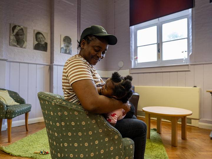 Woman sitting in a green armchair in a living room breastfeeding her child.