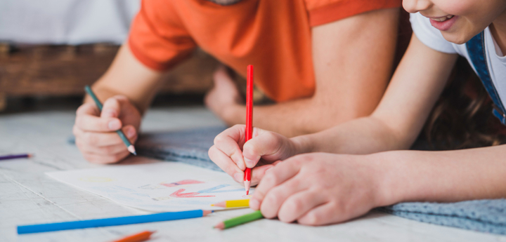 Girl and dad lying on the floor and drawing together on a piece of paper