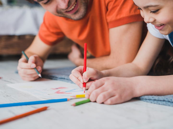 Girl and dad lying on the floor and drawing together on a piece of paper