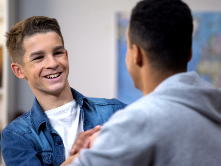 Two teenage boys smiling at one another and shaking hands.