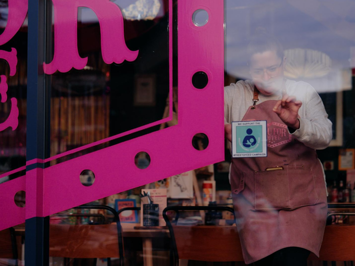 Woman sticking a Free to Feed sticker inside a window of a business