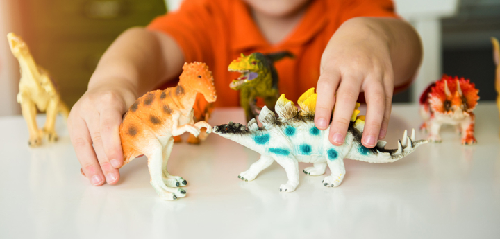 Boy in background holding 2 dinosaurs and playing with them together