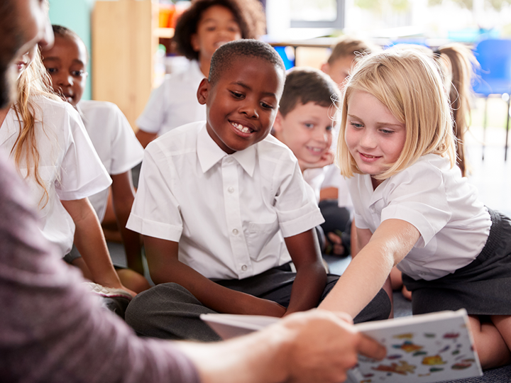 Children in a class looking at a book held by a teacher.