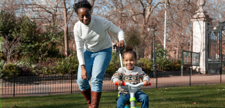 Mother pushing child through park on tricycle