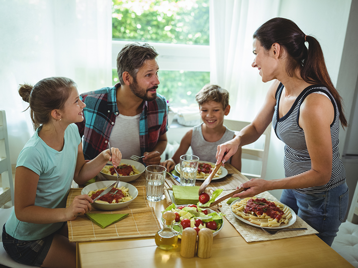 2 adults and 2 children sitting around a dining table. One adult is serving up food. Everyone is smiling.