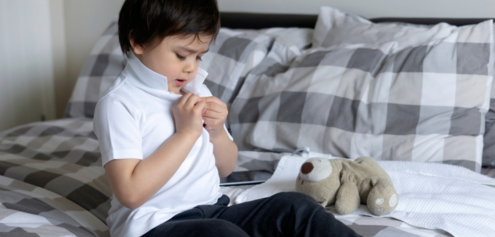 Young boy sitting on a bed buttoning up his white polo-shirt.