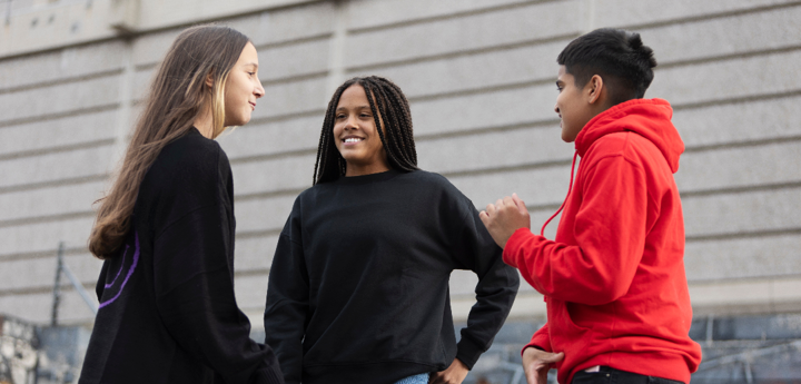 Group of 3 teenagers talking and smiling outside near a graffitied wall.