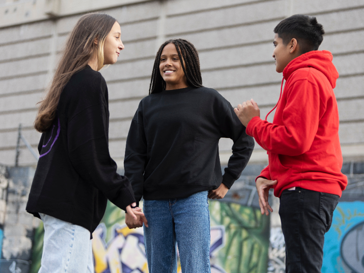 Group of 3 teenagers talking and smiling outside near a graffitied wall.