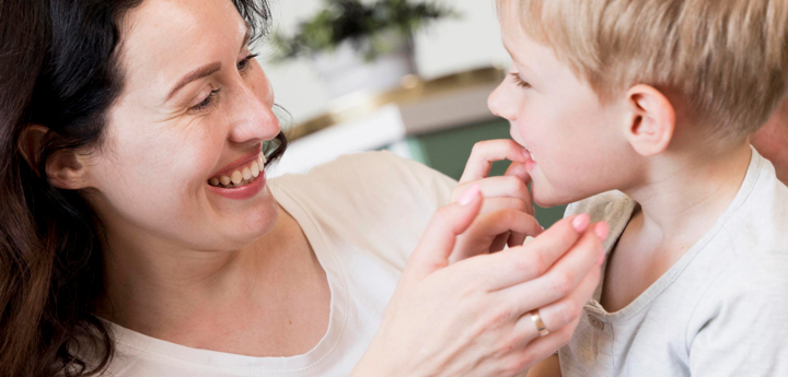Young boy talking to his mum with his finger near his mouth. The mum is smiling and looking at him.