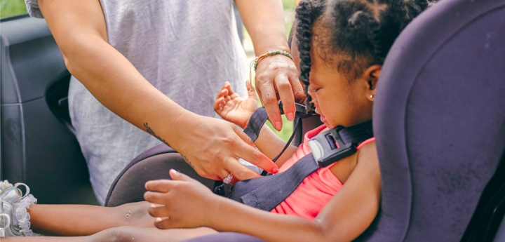 Child being clipped into a forward-facing car seat by adult