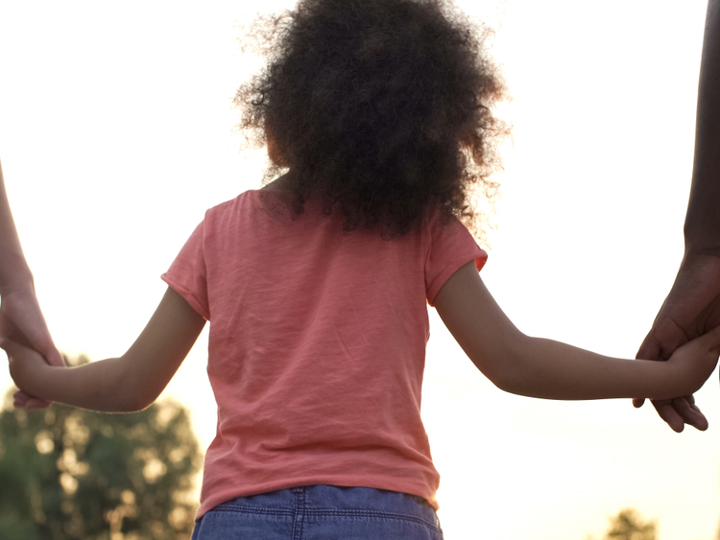 Young girl walking holding hands with 2 adults either side.