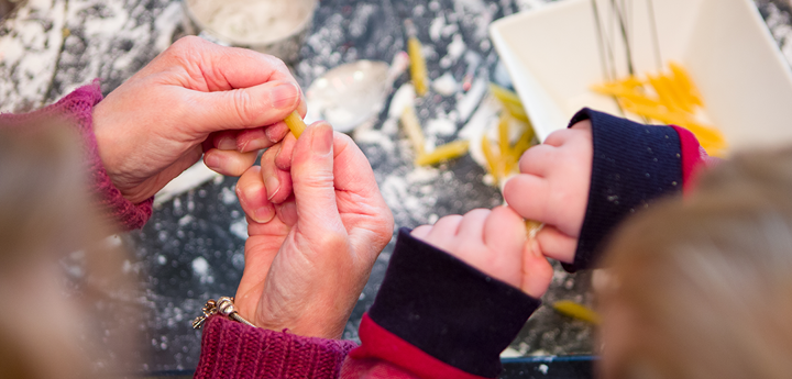 Showing only their hands. Adult and child playing with food. The background is a messy table covered with flour and pasta