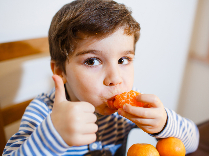 Young boy eating an orange and doing a thumbs up gesture