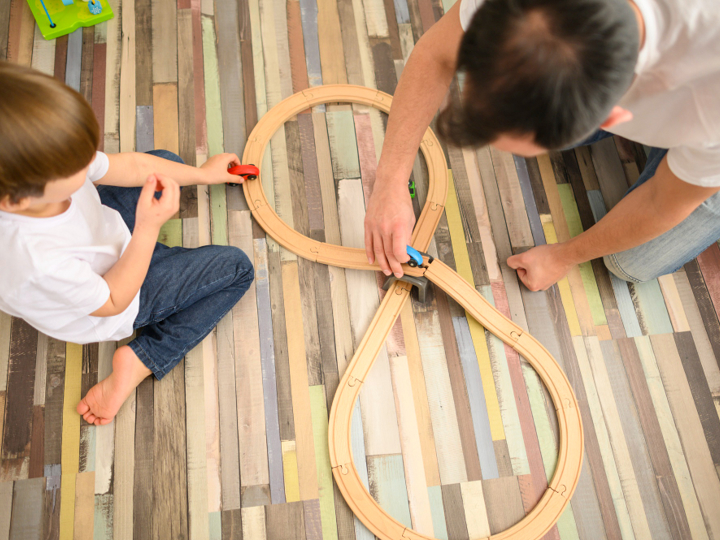 Aerial shot of a young boy and adult man playing with toy cars on a wooden track